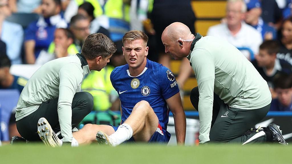 Liam Delap sitting on football pitch, injured for Chelsea