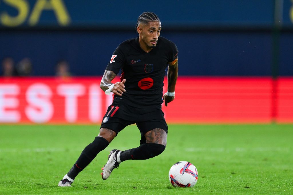 Raphinha in a black Barcelona shirt running with the ball