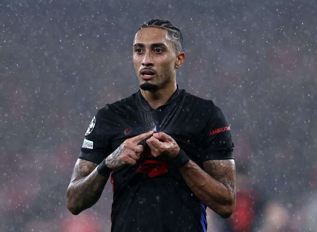 Raphinha pointing at the Barcelona logo on a rainy Champions League night