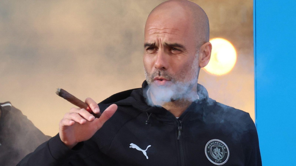 Pep Guardiola smoking a cigar in a Manchester City jacket